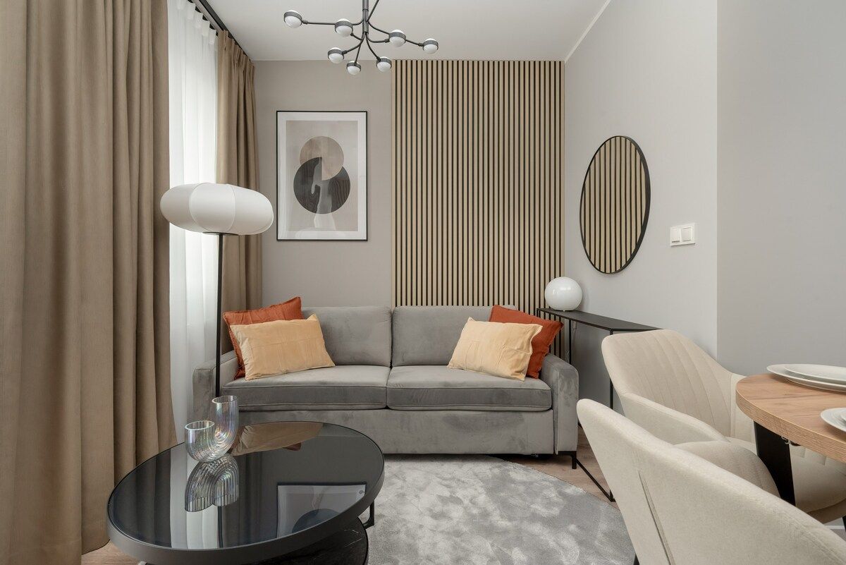 A modern living room with a grey sofa, a round glass coffee table, and a beige armchair.