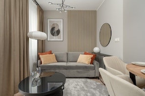 A modern living room with a grey sofa, a round glass coffee table, and a beige armchair.