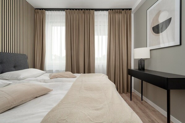 A hotel room with a bed, curtains, a bedside table, and a wall-mounted lamp.