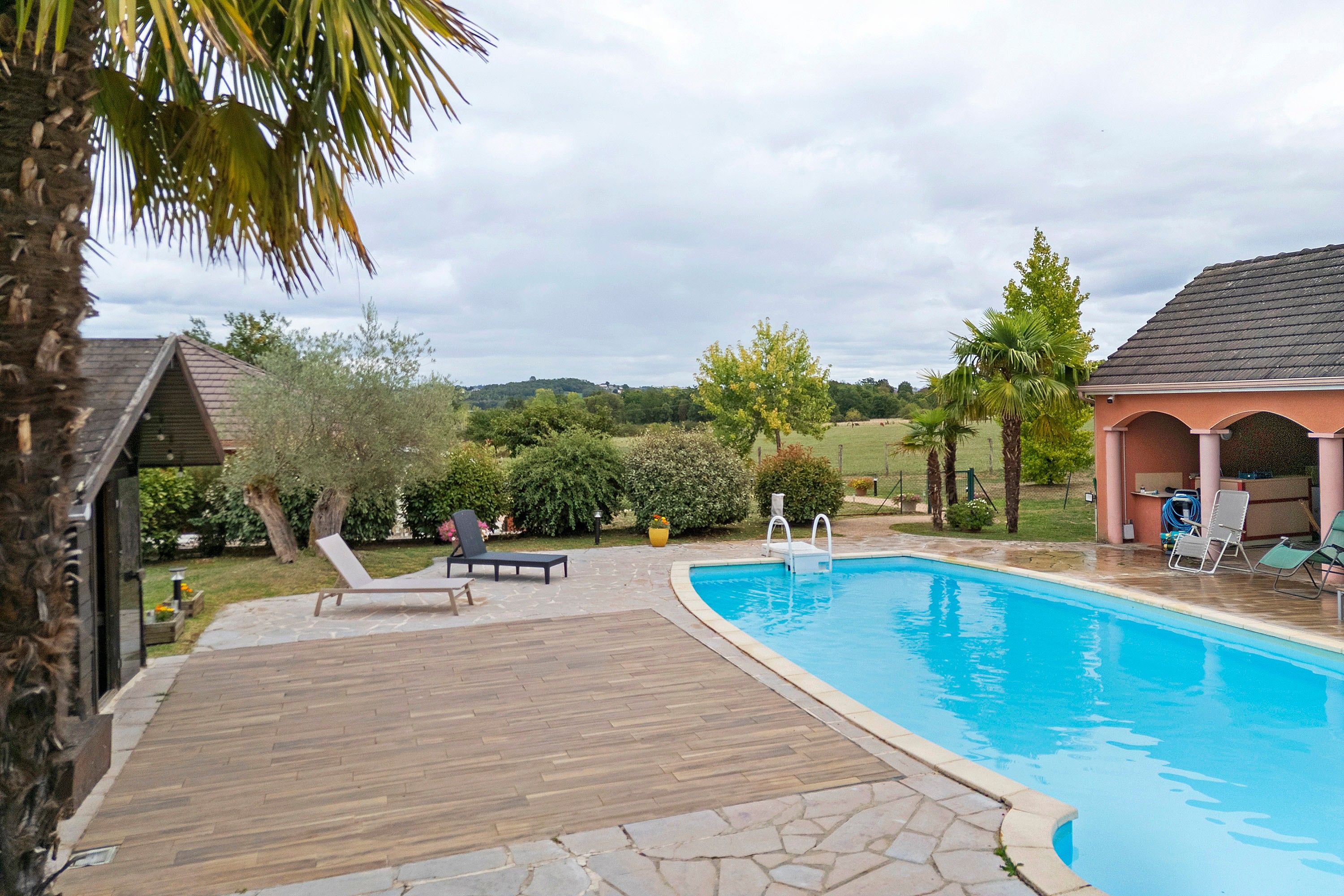 Une piscine dotée d’une terrasse en bois, de chaises longues et d’un espace couvert avec un toit.