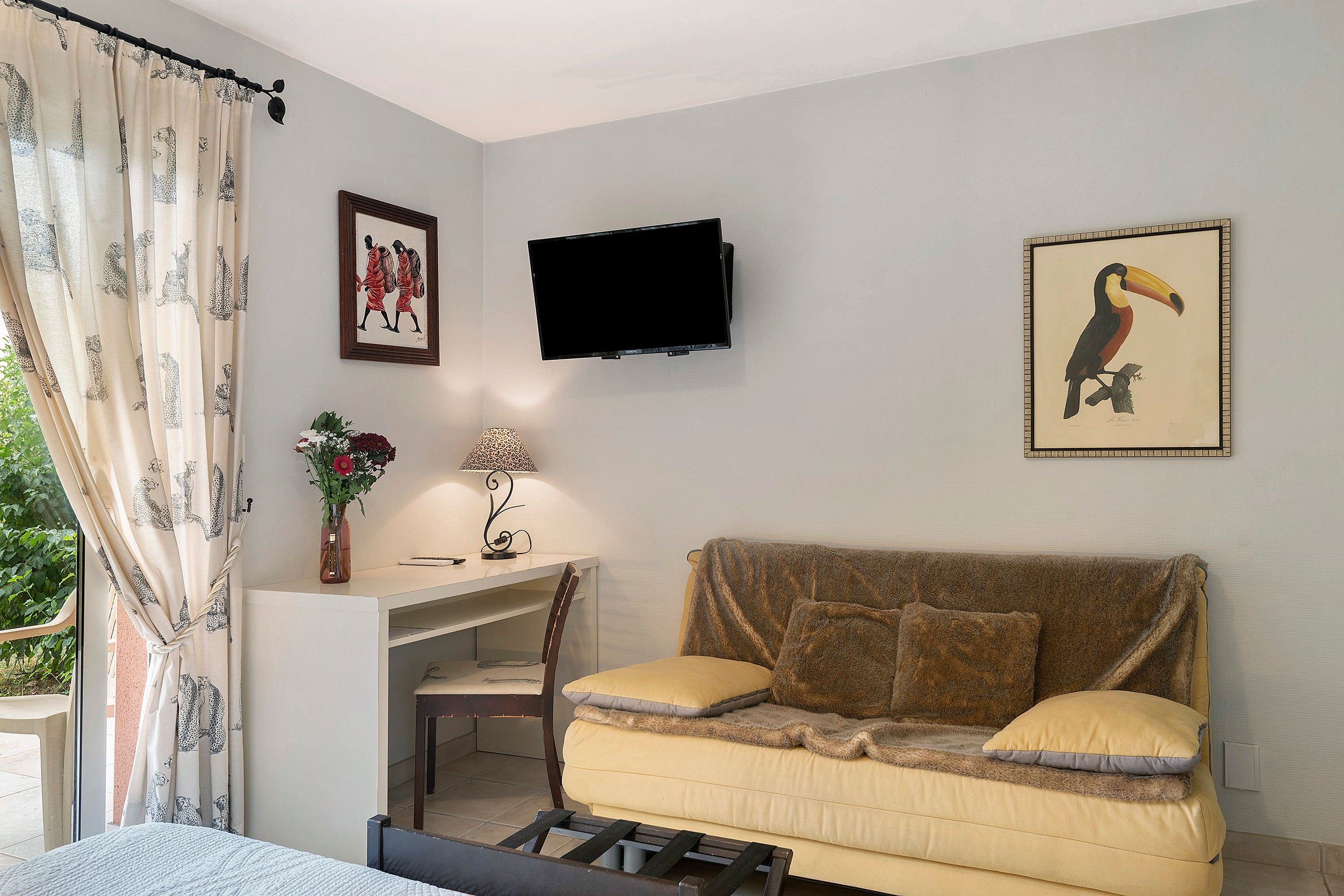 Une pièce comprenant un lit, un canapé, un bureau avec une chaise, un téléviseur fixé au mur et une fenêtre avec des rideaux.