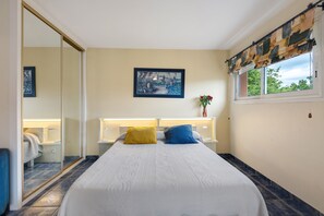 Un dormitorio con cama, mesitas de noche, un espejo, una ventana con cortinas y un cuadro en la pared.