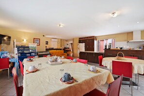 Un comedor con mesas dispuestas para una comida, una cocina al fondo y una sala de estar con sofá.