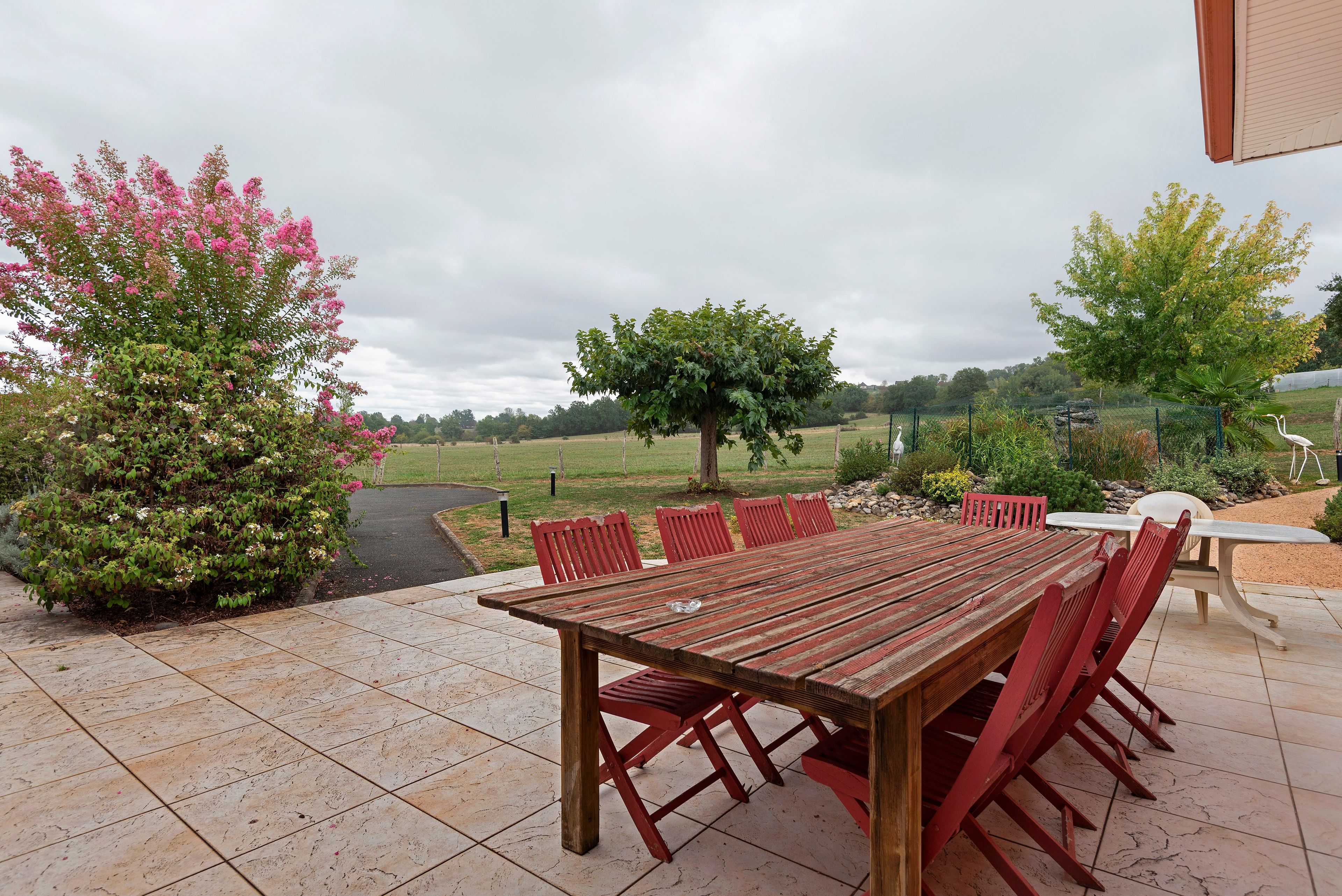 Une terrasse extérieure avec une table et des chaises en bois, entourée de verdure et offrant une vue sur la campagne.