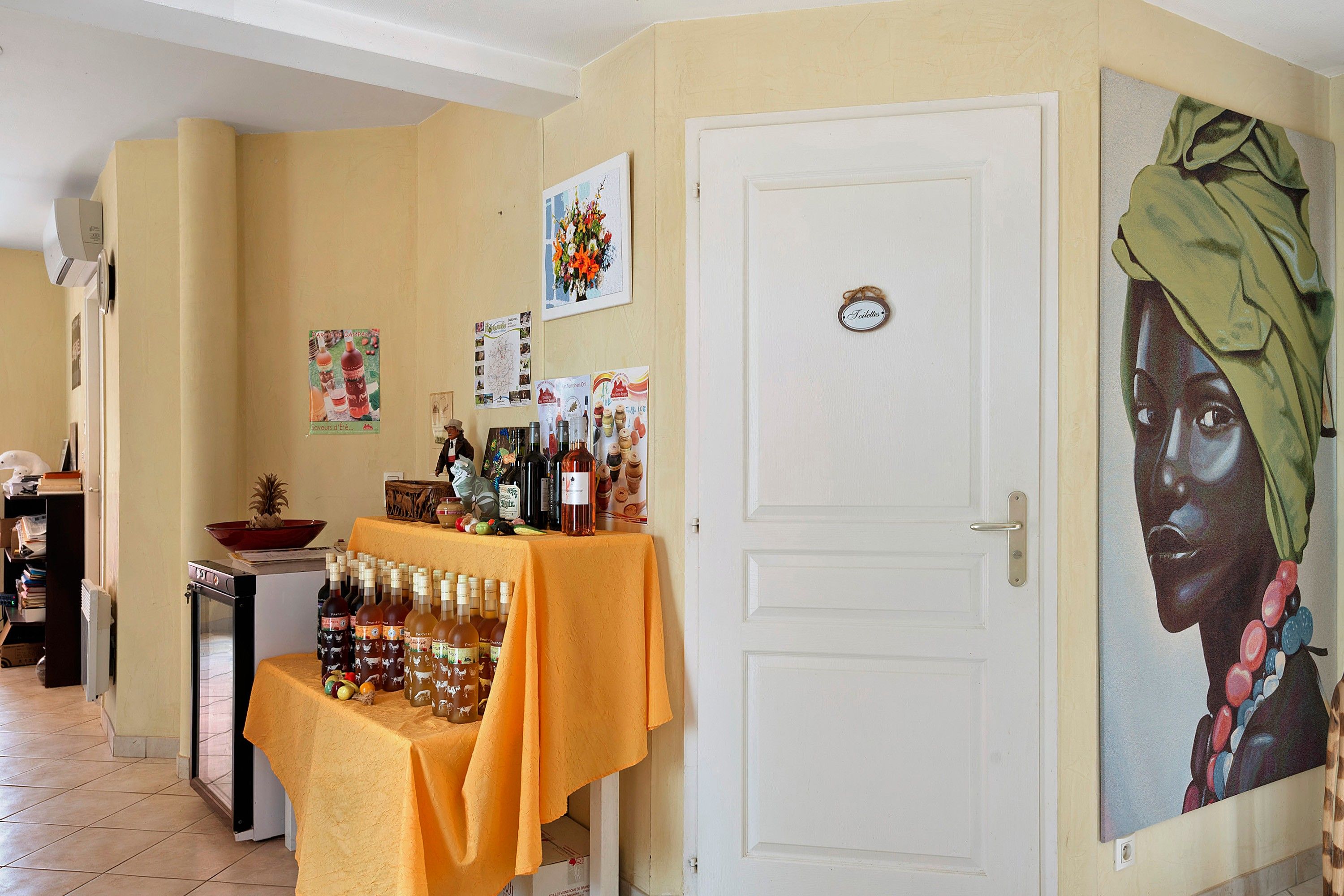 Een kamer met een witte deur, een tafel met flessen en een schilderij aan de muur.