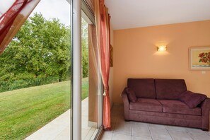 A room with a sliding glass door leading to a garden, a sofa, and a wall-mounted light fixture. - Bed and Breakfast 'La Coloniale - Prune' with Private Pool, Wi-Fi and Air Conditioning (Varetz)