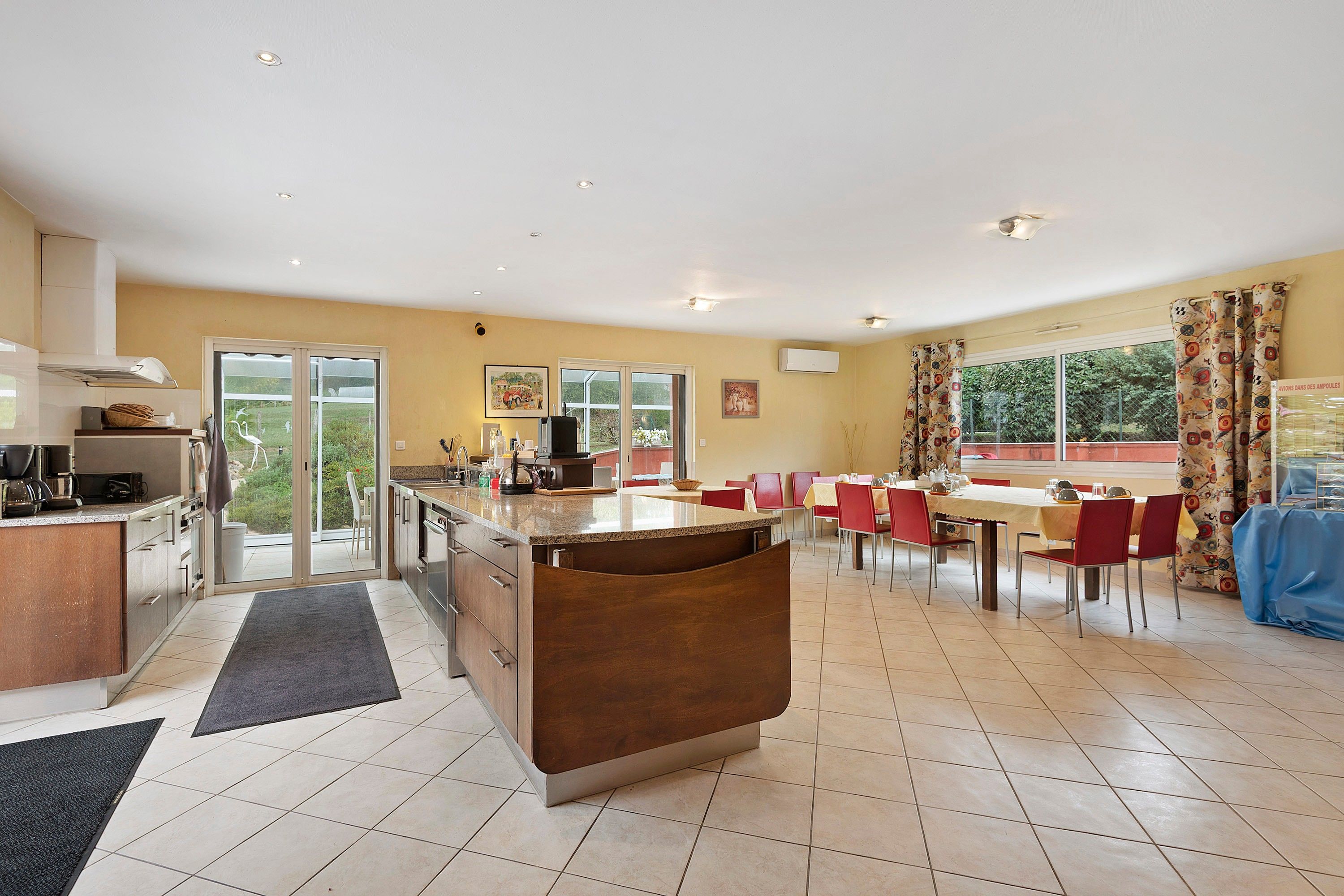 A modern kitchen with a central island, a dining area with red chairs, and a large window providing natural light.
