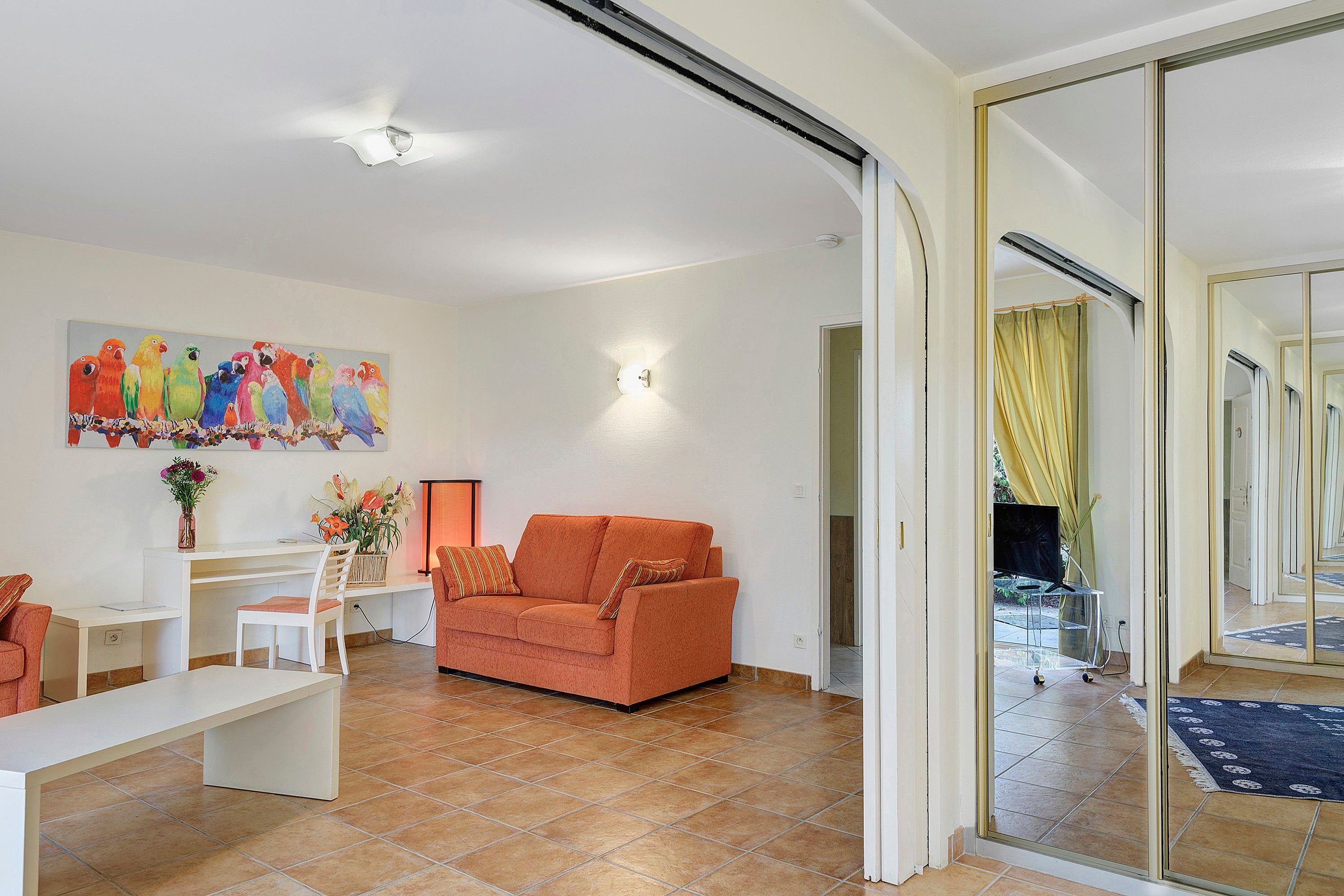 A living room with a sofa, a coffee table, a painting, and a sliding glass door leading to a balcony.