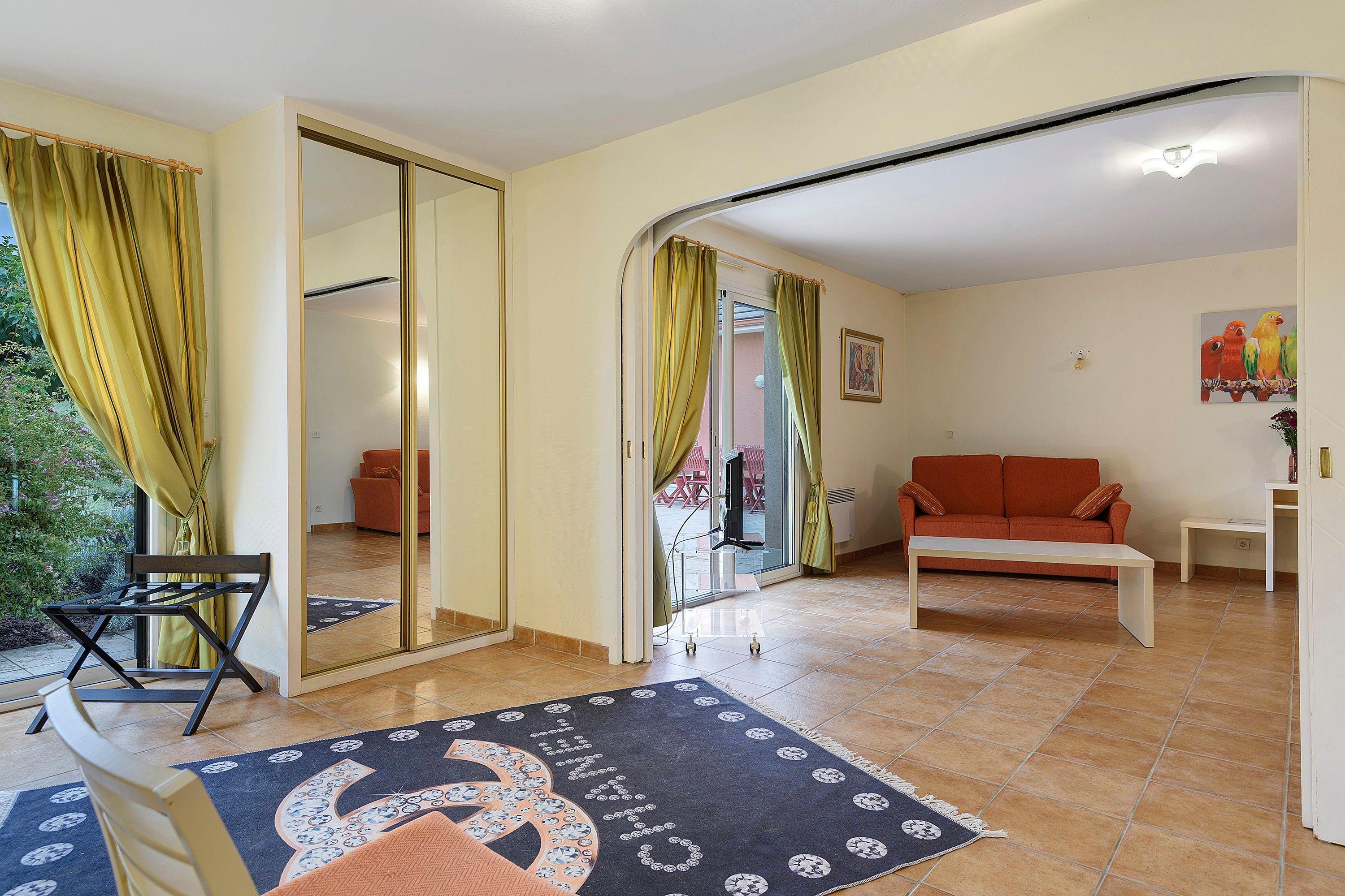 Un salon comprenant un canapé, une table basse et un fauteuil. Une porte coulissante donne accès à un balcon.