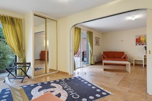 Sala de estar con sofá, mesa de centro y sillón. Posee un ventanal corredizo que da a un balcón.