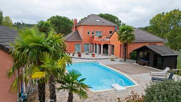 Une maison à deux étages avec une piscine, entourée de palmiers et de plantes en pot.