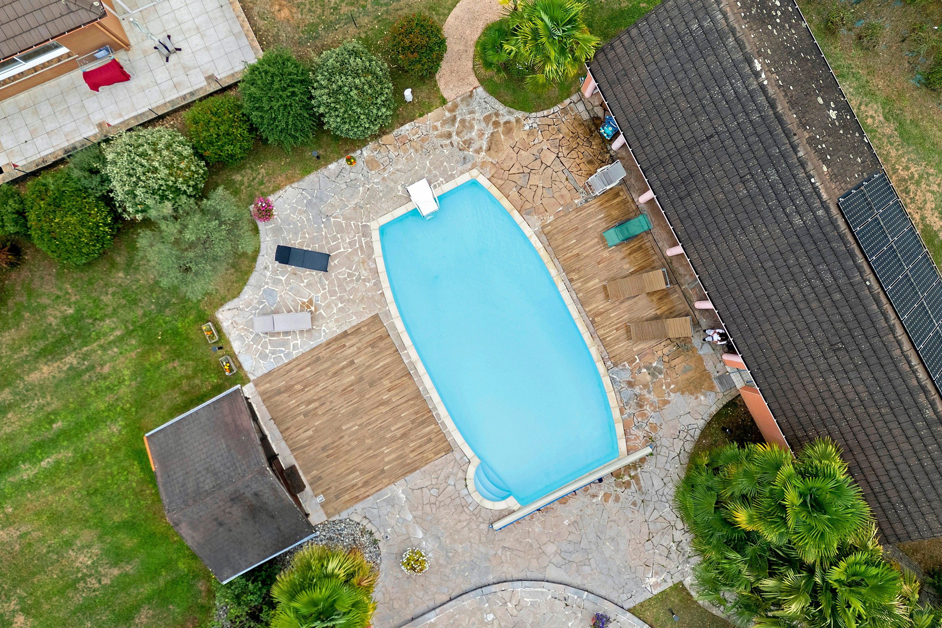 Vue aérienne d’une propriété résidentielle dotée d’une piscine, d’un patio couvert et d’un jardin.