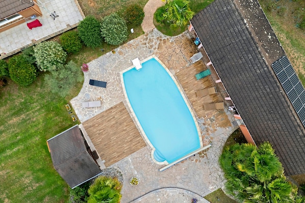 Vista aérea de una propiedad residencial con piscina, patio cubierto y jardín.