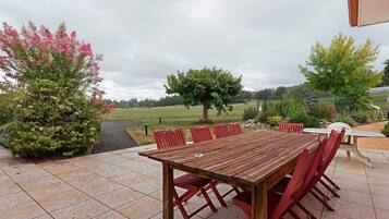 Un patio al aire libre con una mesa y sillas de madera, rodeado de vegetación y vistas al campo.