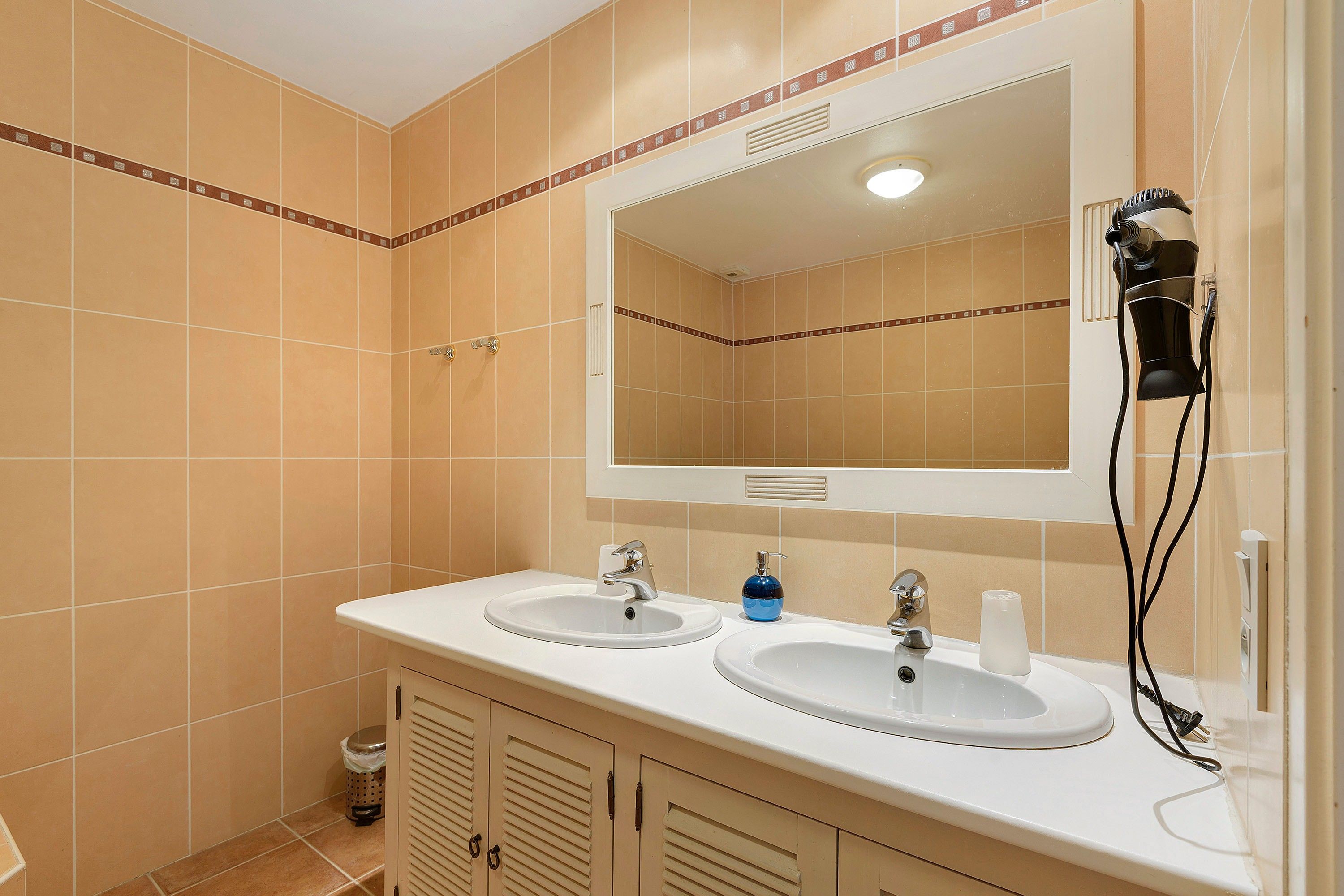 Een badkamer met twee wastafels, een spiegel, een haardroger en een prullenbak.