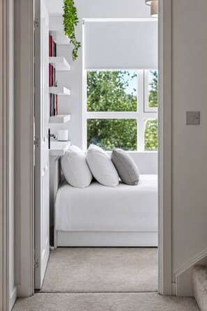 A bedroom with a bed, pillows, a white wall, a window, and a bookshelf. - Stylish 3BR Home Parking EV Sleeps 6 (Harrow)