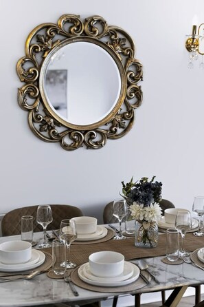 A dining table set with white plates, bowls, and cutlery, a vase with flowers, and a gold-framed mirror on the wall. - Stylish 3BR Home Parking EV Sleeps 6 (Harrow)