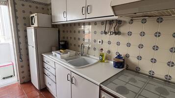 A compact kitchen with white cabinets, a built-in oven, a microwave, and a sink.