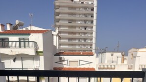 Un balcón con una mesa redonda y sillas, piso de baldosas y vistas a edificios cercanos.
