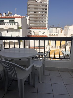 A balcony with a round table and chairs, a tiled floor, and a view of adjacent buildings. - Cantinho de Mar Holiday Home (Monte Gordo)