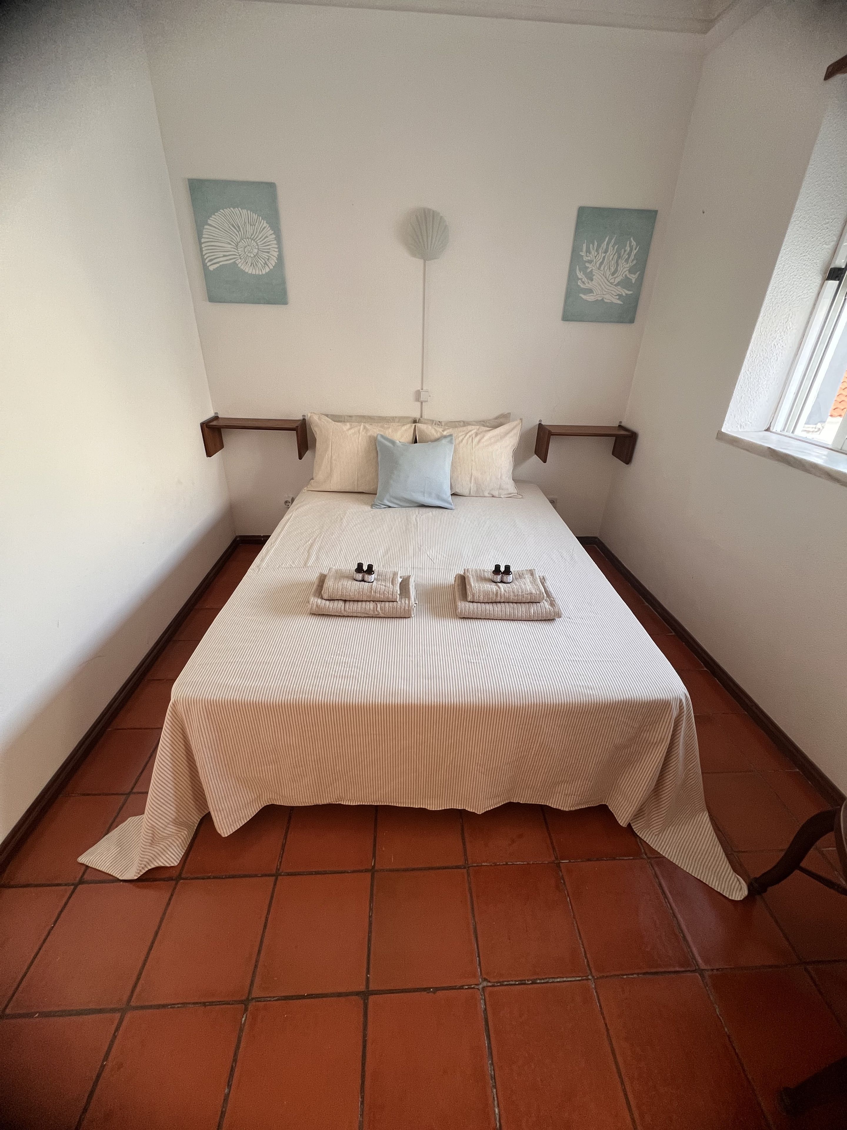 Una cama con una colcha a rayas, dos almohadas y una mesita de noche con una botella y una caja de pañuelos.