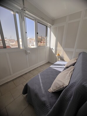 A bedroom with a bed, a nightstand, and a window with a view of buildings. - Cantinho de Mar Holiday Home (Monte Gordo)