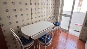 Un comedor con mesa y sillas blancas, papel tapiz estampado y vista a través de un ventanal.