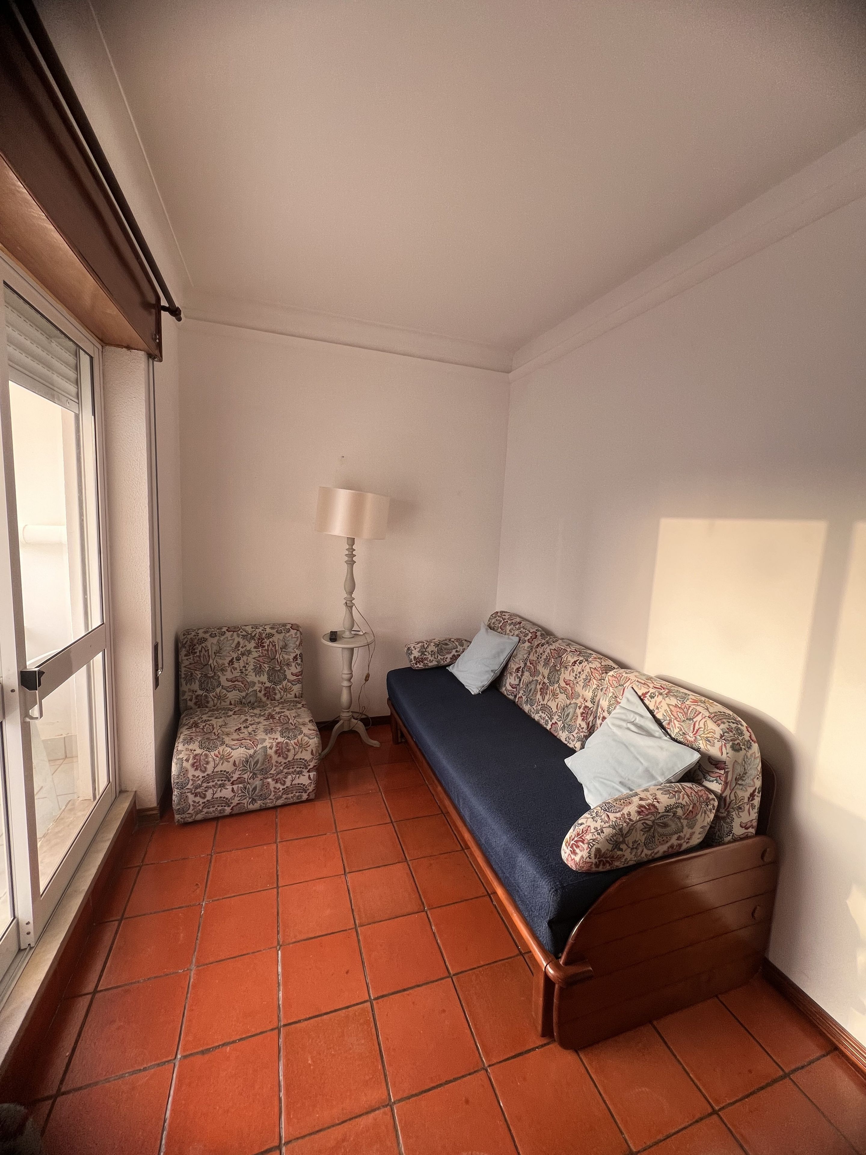 A small room with a sofa, a chair, a lamp, and a window.