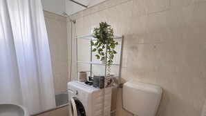 Un baño pequeño con lavadora, inodoro y un estante con una planta.