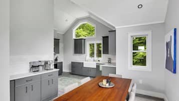 Una cocina moderna con armarios grises, una mesa de comedor de madera y vistas a zonas verdes por las ventanas.