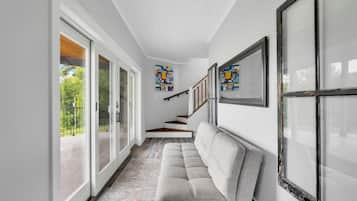 Un pasillo con un sofá gris, una escalera y vistas al exterior con vegetación.