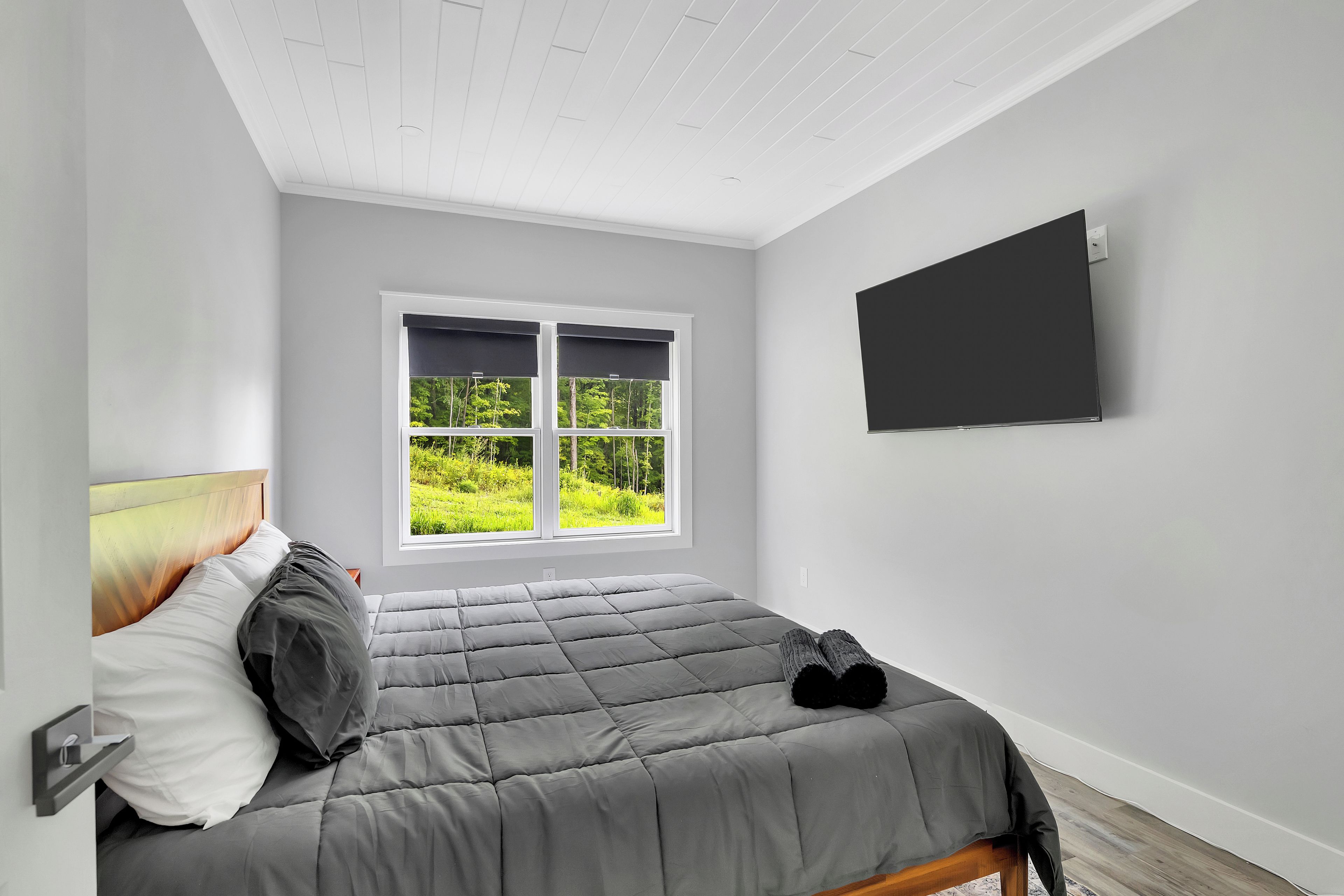 Un dormitorio con cama, ventana con vista a la vegetación y televisor de pantalla plana montado en la pared.