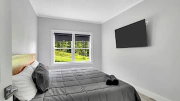 Un dormitorio con cama, ventana con vista a la vegetación y televisor de pantalla plana montado en la pared.