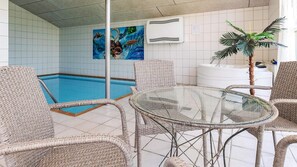 Ein Poolbereich mit Korbstühlen, einem Glastisch, einem Gemälde mit einer Surf Szene und einer weißen Klimaanlage.