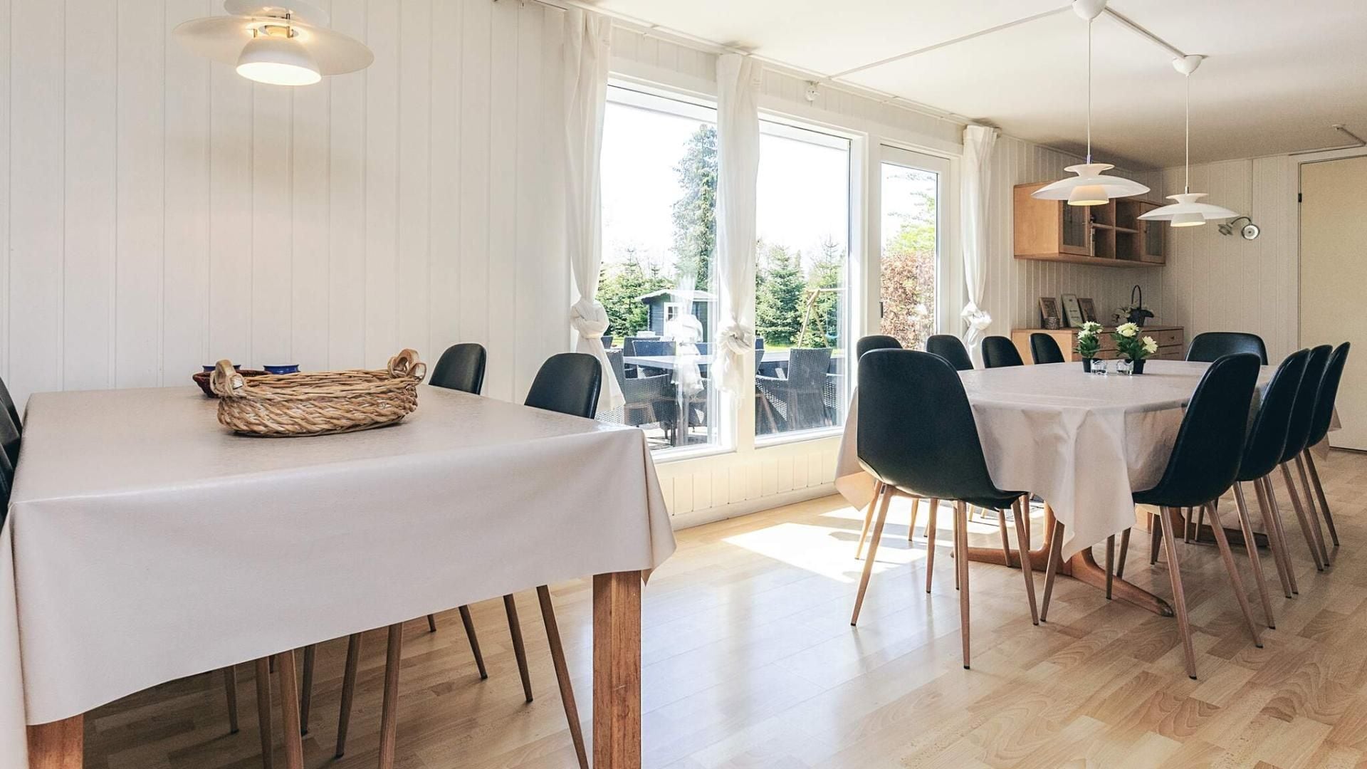 A dining area with a table set for six, wooden flooring, and a view of the outdoors through large windows.