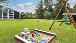 Ein Garten mit Sandkasten, Schaukel und Spielhäuschen.