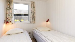 Ein Zimmer mit zwei Betten, einem Fenster mit floralem Vorhang und einer roten Wandleuchte.