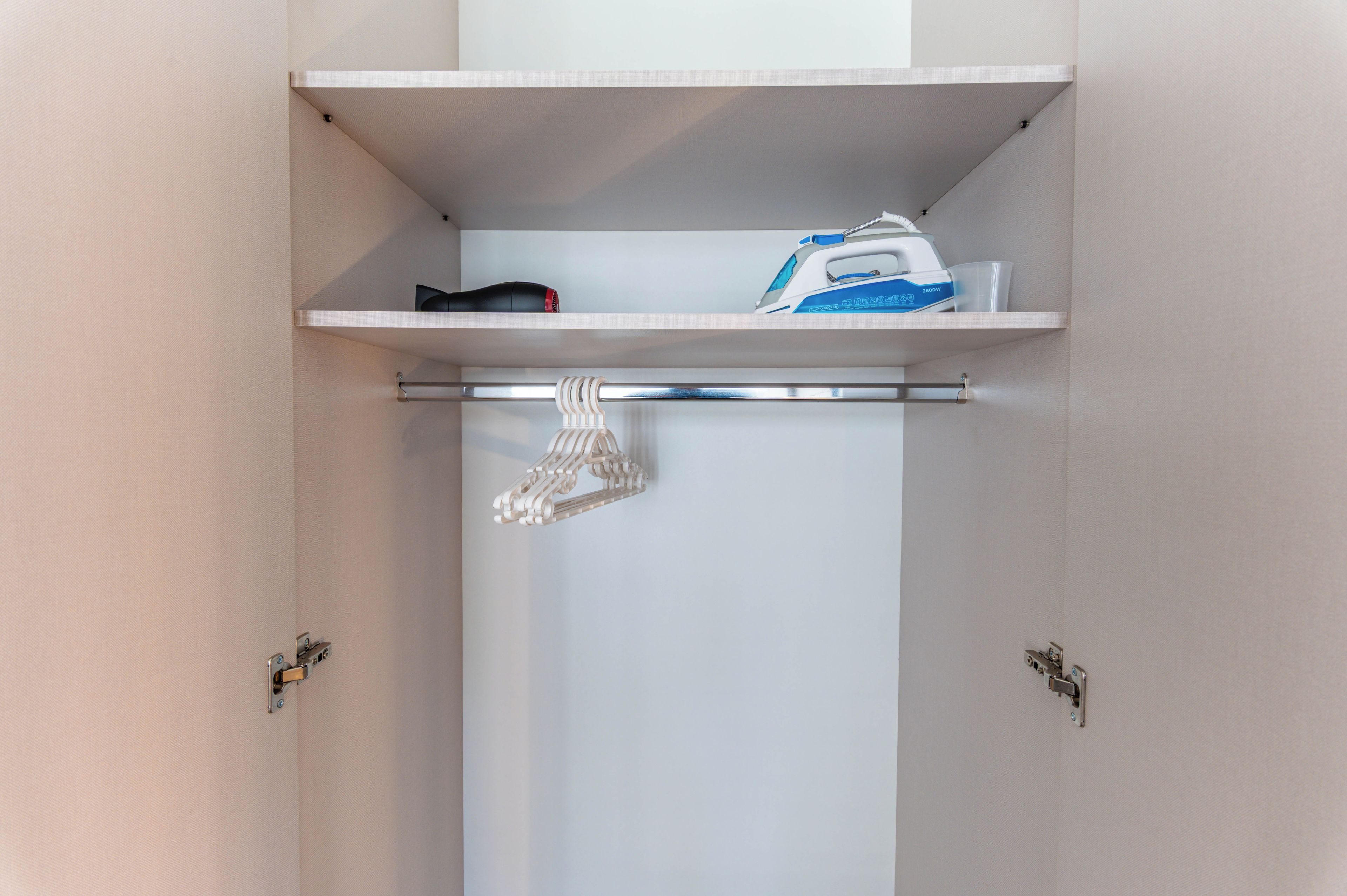 A closet with a hanging shoe rack and an ironing board with an iron and board.