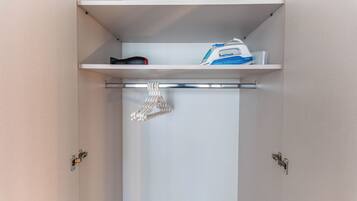 A closet with a hanging shoe rack and an ironing board with an iron and board.
