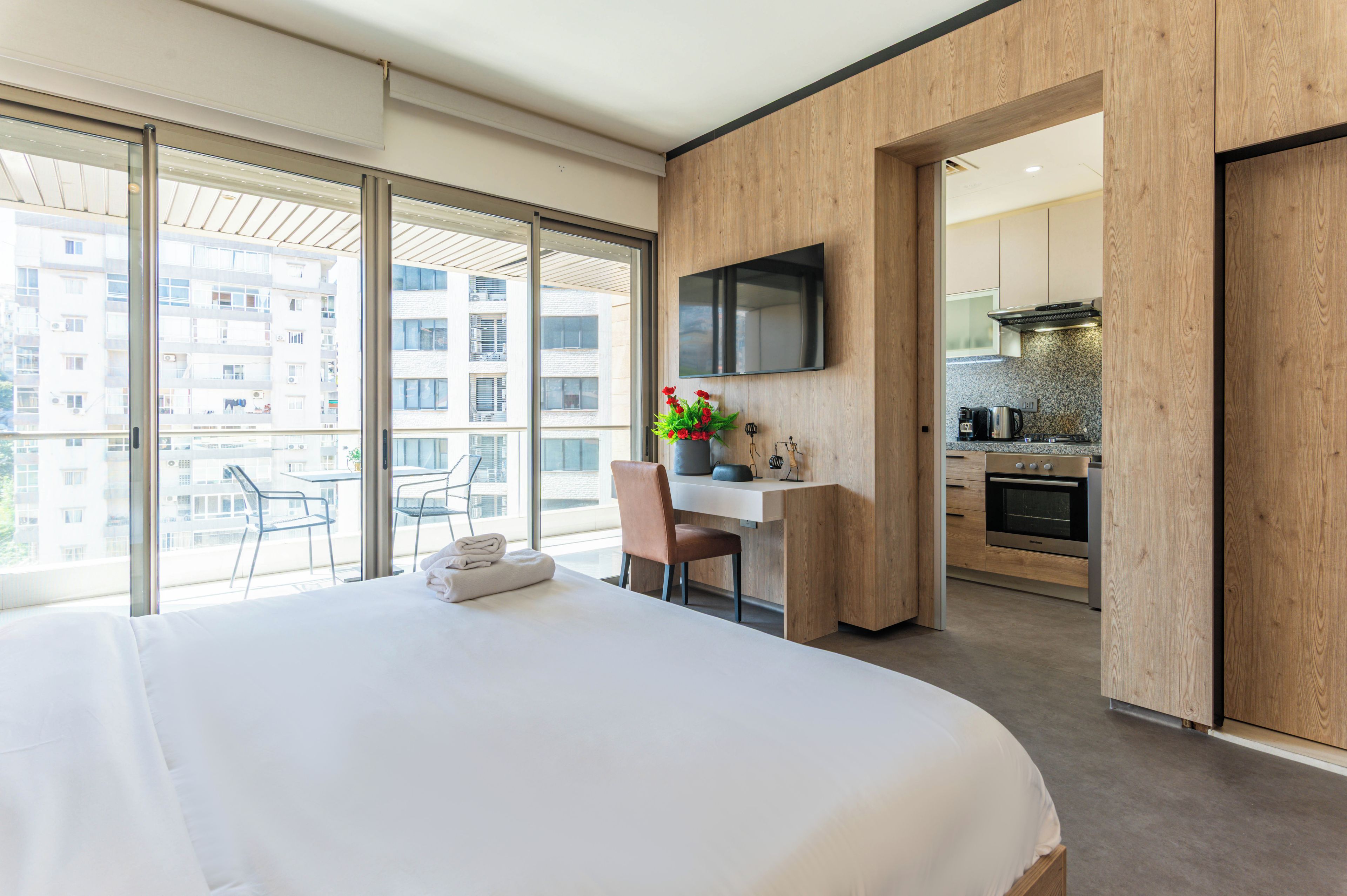 Ein modernes Hotelzimmer mit einem großen Bett, einem Schreibtisch, einem Flachbildfernseher und Blick auf die Stadt durch große Fenster.