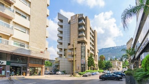 A multi-story building with balconies, a sign for 'AAA COMFORT', and a street with parked cars and greenery. - Elara Studio & Balcony in Jounieh (Jounieh)