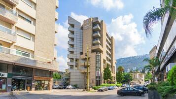 Un edificio de varios pisos con balcones, un letrero que dice 'AAA COMFORT' y una calle con coches estacionados y vegetación.