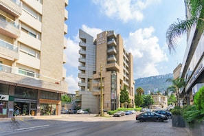 A multi-story building with balconies, a sign for 'AAA COMFORT', and a street with parked cars and greenery. - Elara Studio & Balcony in Jounieh (Jounieh)