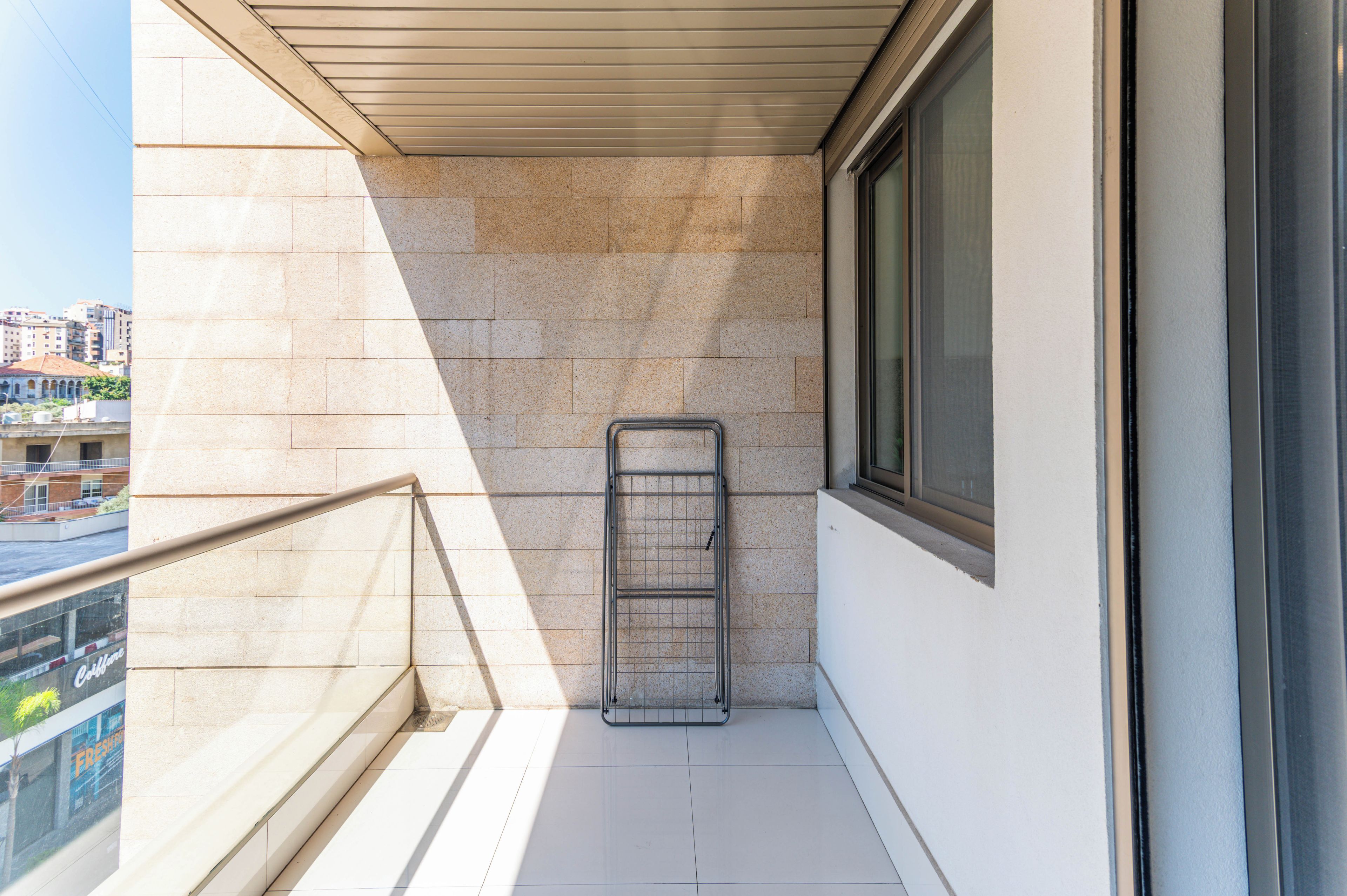Un balcón con un tendedero de metal, una ventana y vistas a edificios.