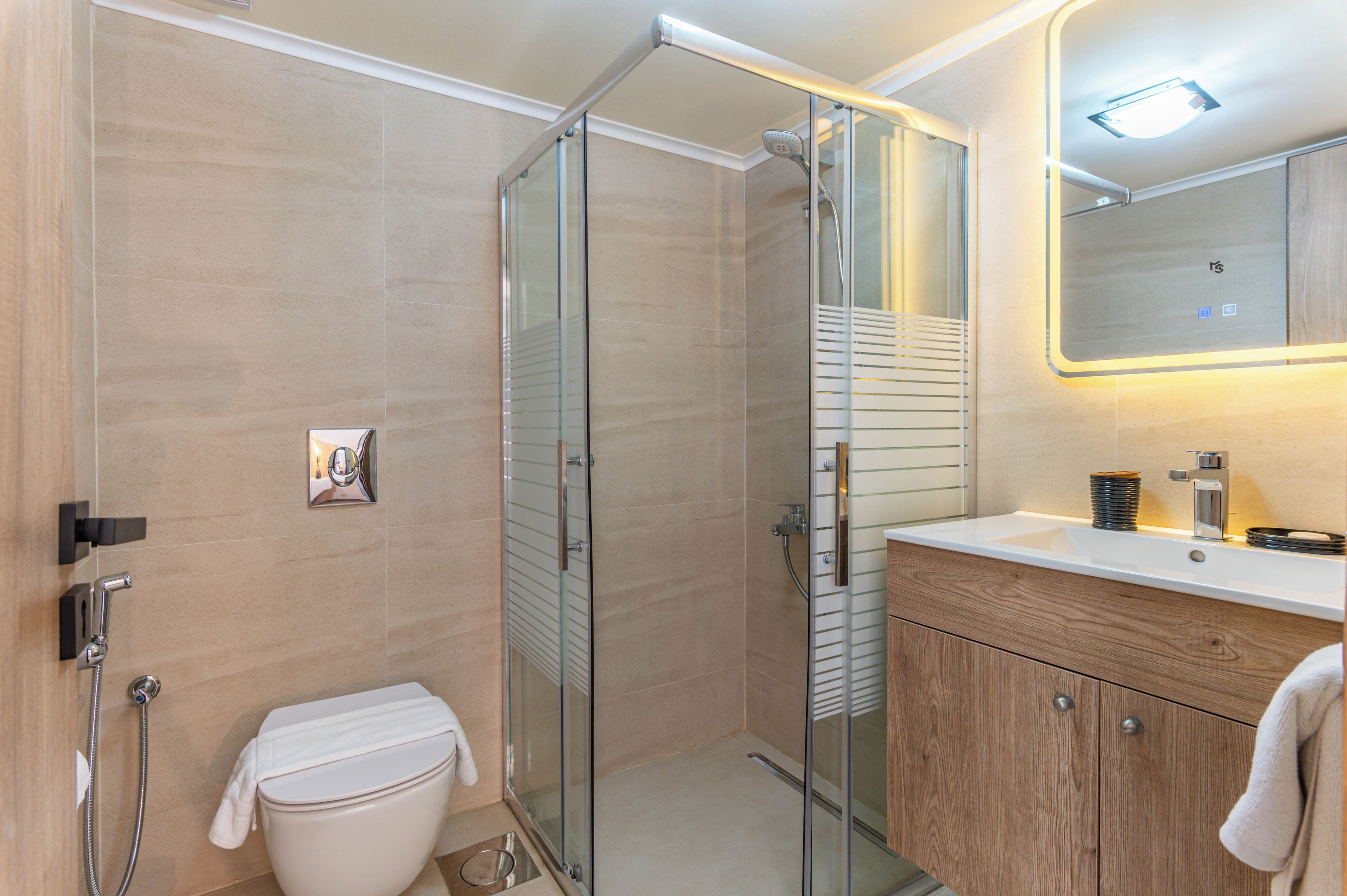 A modern bathroom with a glass-enclosed shower, a toilet, a sink with a mirror, and wooden cabinetry.