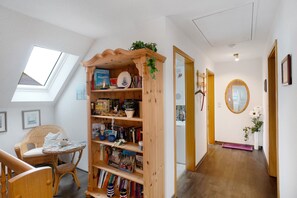 A room with a wooden bookshelf, a wicker chair, a small table with a lamp, and a skylight. - Apartment 'Warftoase' (Krummhörn Grimersum)