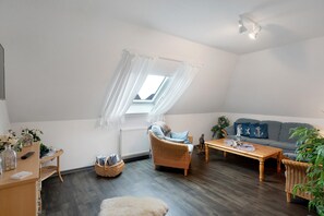 Een gezellig loft slaapkamer met schuine wand, dakraam, een bank, een houten salontafel en rieten meubels.