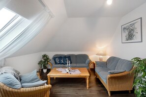 Een gezellige woonkamer met een bank, twee fauteuils, een salontafel en een potplant.