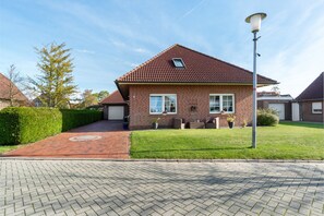 Een woonhuis met een bakstenen gevel, een pannendak, een verharde oprit en een lantaarnpaal.
