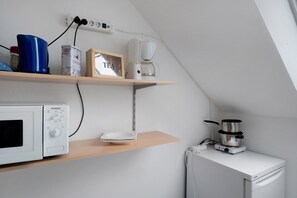 A kitchenette with a microwave, coffee maker, and a small stove. There are shelves with a coffee box and a framed picture. - Apartment 'Warftoase' (Krummhörn Grimersum)
